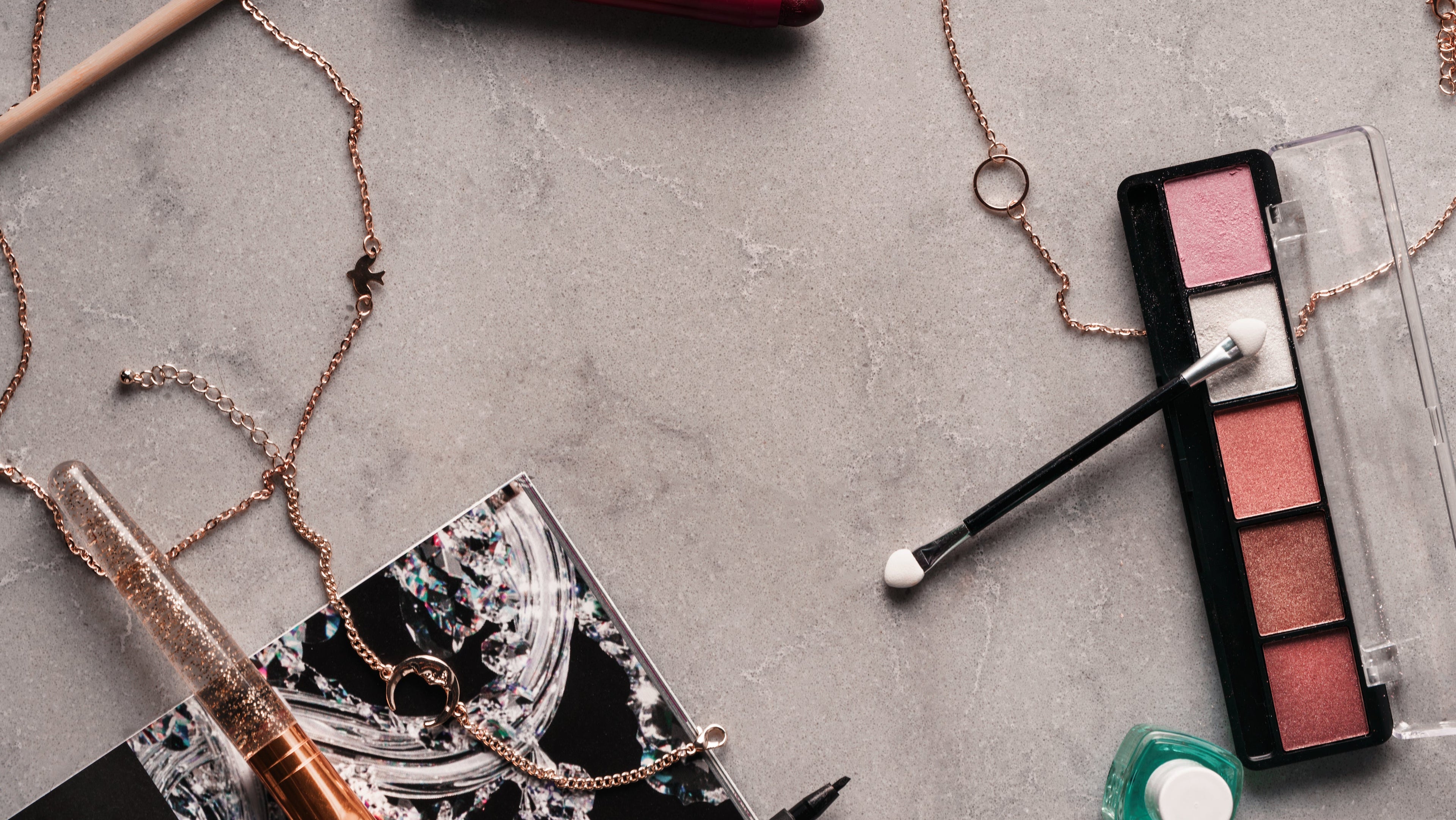 Makeup items including a brush, palette, and lip products on a gray surface.