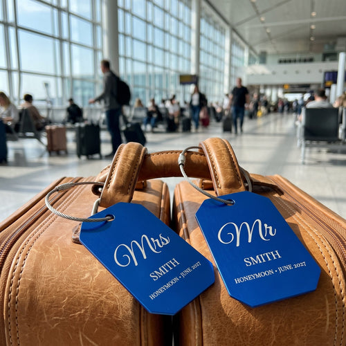 A pair of blue Mr and Mrs Smith honeymoon luggage tags on tan suitcases at the airport