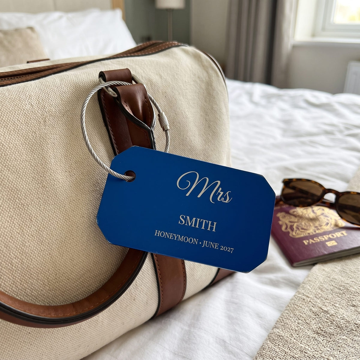 Engraved blue luggage tag on a cream weekend bag with passports