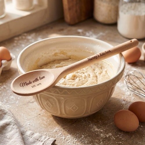 Engraved beech wooden spoon reading Nanny's Kitchen resting on a mixing bowl of cake batter