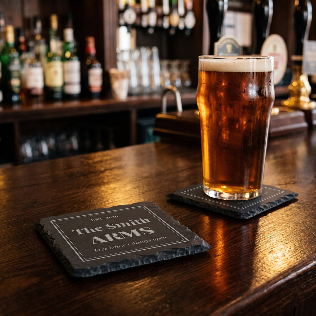 Pub sign slate coasters engraved The Smith Arms Est. 2019 on a home bar with a pint of ale